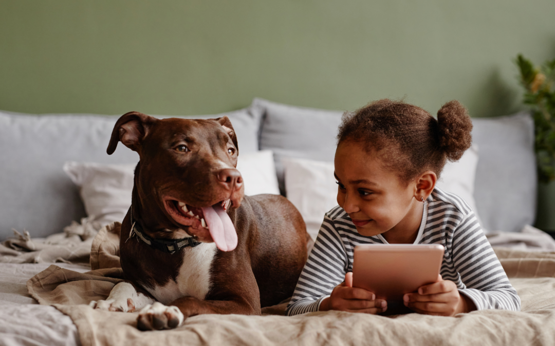 photograph of a dog laying beside a young girl who is smiling with a book in hand