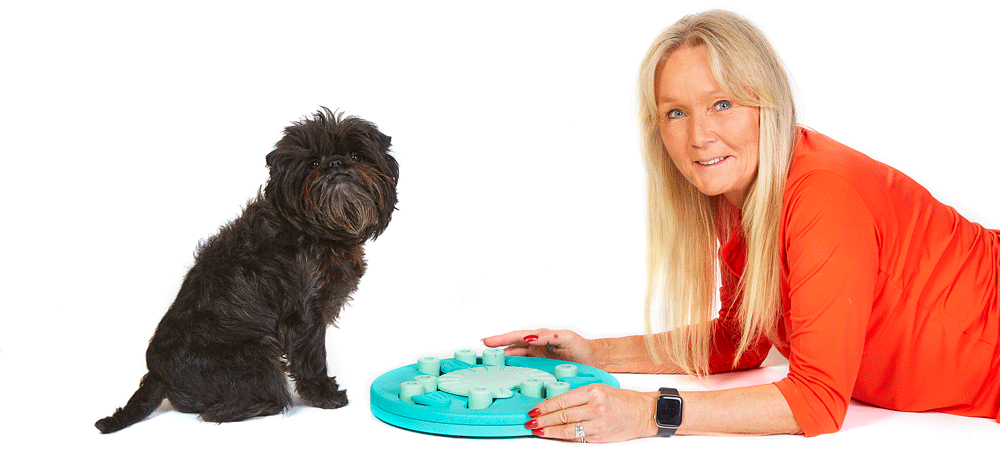 Nina Ottosson pictured with a small dark dog with a canine puzzle toy for enrichment